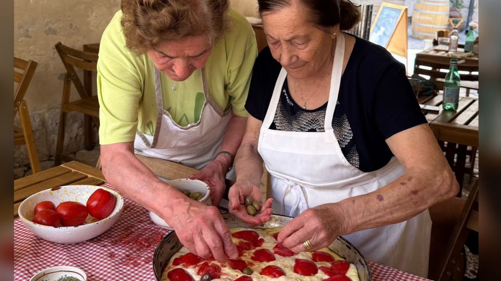 Due donne anziane che preparano la pizza in casa su un tavolo con tovaglia a quadri