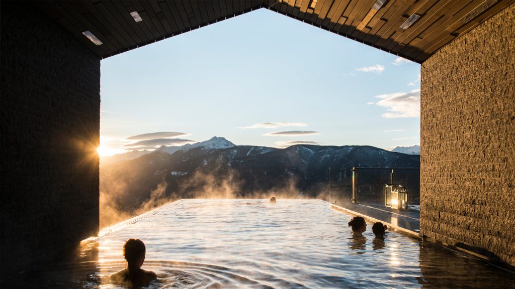 Persone in una piscina termale all'aperto affacciata sulle montagne al tramonto