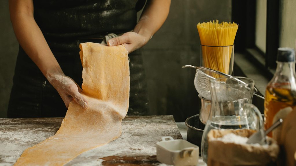 Mani che stendono la sfoglia di pasta fresca su un piano infarinato