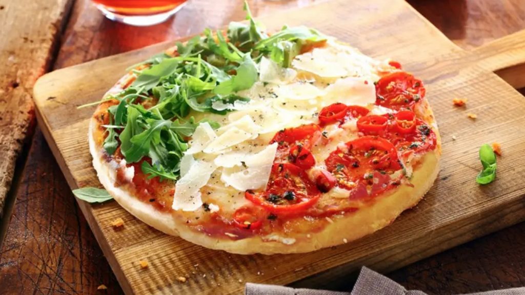 Pizza con rucola, mozzarella e pomodoro a forma di bandiera italiana su un tagliere