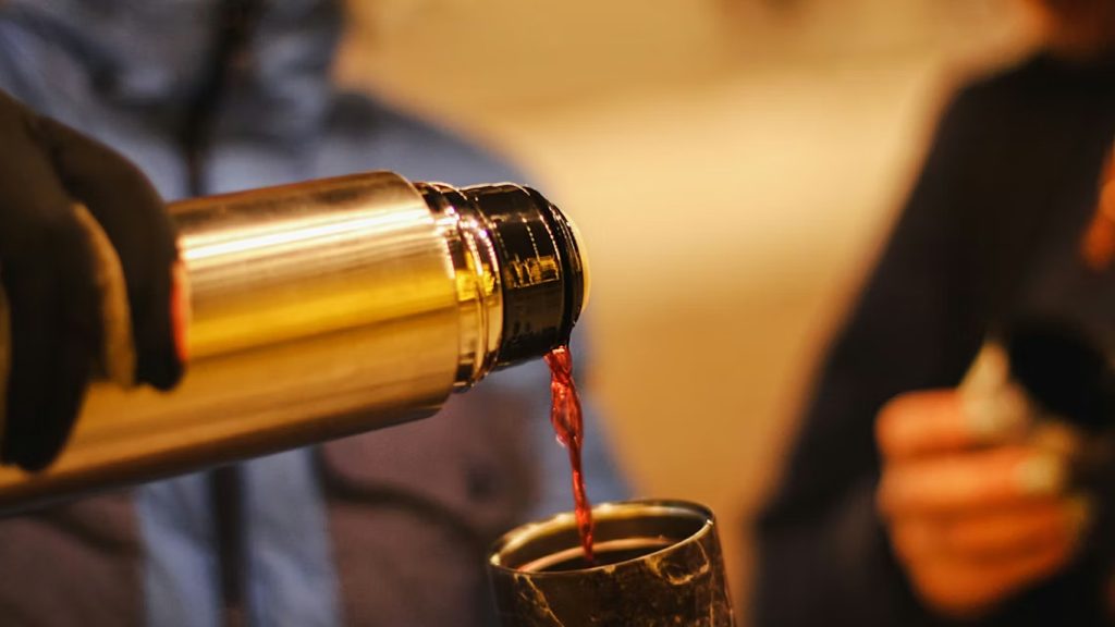 Vino rosso versato da un thermos dorato in un bicchiere