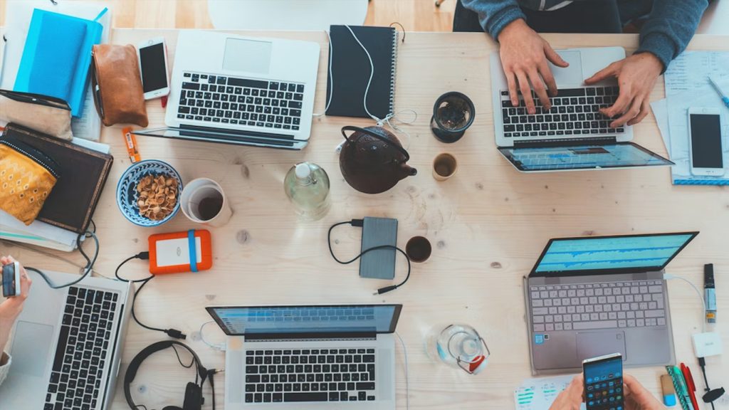 Scrivania vista dall'alto con computer portatili, smartphone e tazze