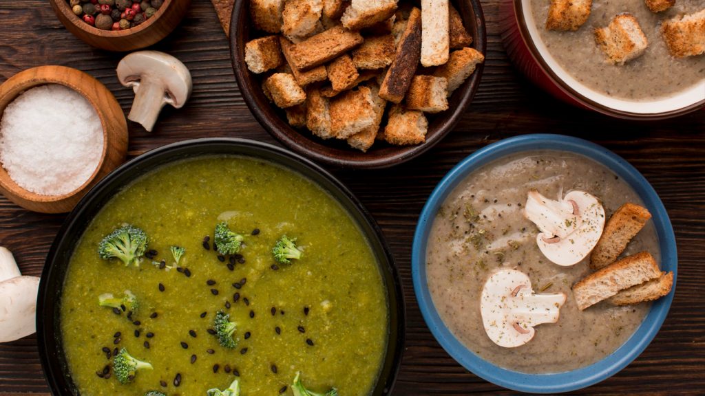 Ciotole di zuppe e vellutate con crostini e funghi su un tavolo scuro
