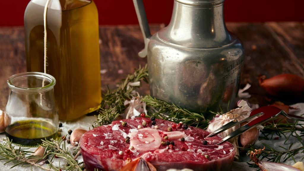 Ampolla d'olio, caraffa e carne cruda con erbe su un tavolo rustico
