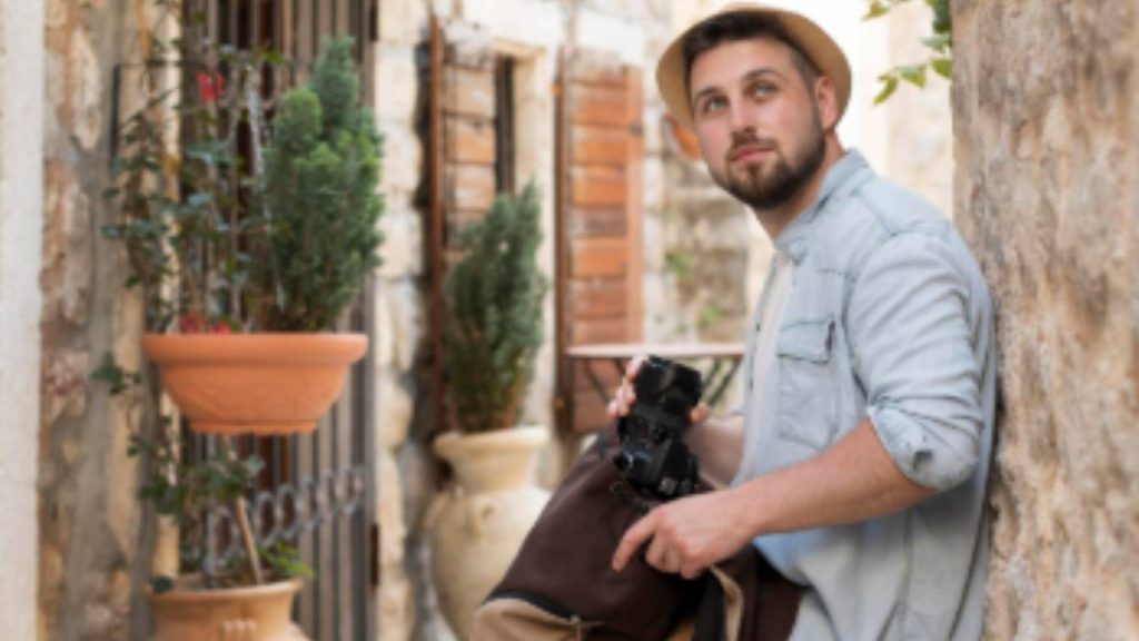 Fotografo con cappello che scatta in un vicolo con fiori