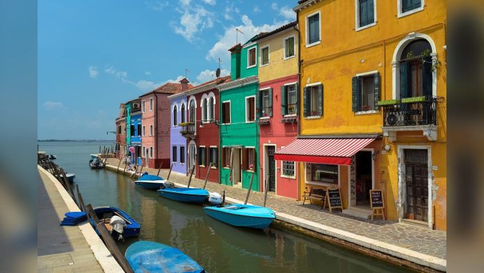 Case dipinte di giallo, verde, rosa e blu lungo un canale di Burano con barche azzurre ormeggiate