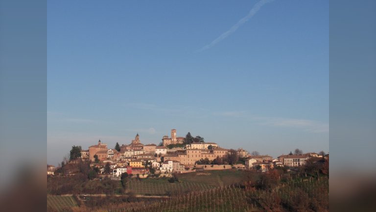 Il borgo di Neive sulla cima della collina, circondato dai vigneti delle Langhe sotto un cielo azzurro